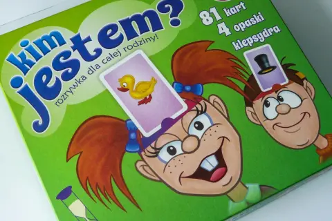 Gra "Kim jestem?" to świetna zabawa dla całej rodziny! Na zielonym tle widać wesołe postacie z kartami na głowach.