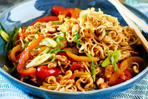 Schüssel mit Nudeln, Paprika, Frühlingszwiebeln und Hühnchen. Ein Teller mit einfachen asiatischen Gerichten, bereit zum Genießen mit Stäbchen.