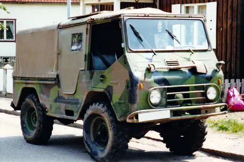 En kamouflerad Volvo L3314 står parkerad framför ett hus.