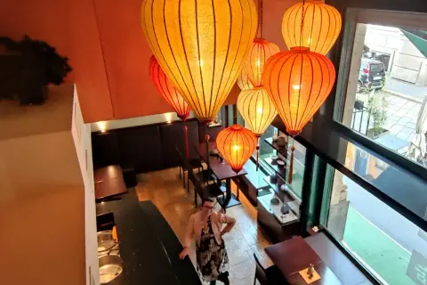 Interno di un ristorante cinese a Milano, illuminato da lanterne orientali. Una donna osserva l'ambiente.