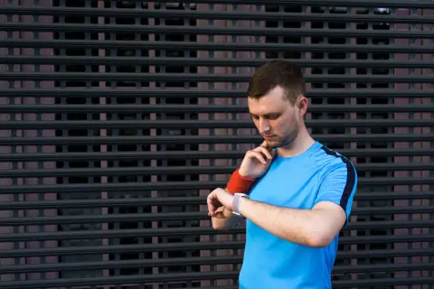 Mężczyzna w sportowej koszulce sprawdza na zegarku tętno spoczynkowe u sportowców.