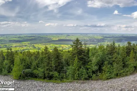 Widok z góry na zielone pola i lasy, idealne na fajne miejsca w świętokrzyskim na weekend. Kamieniste zbocze i chmury na niebie.