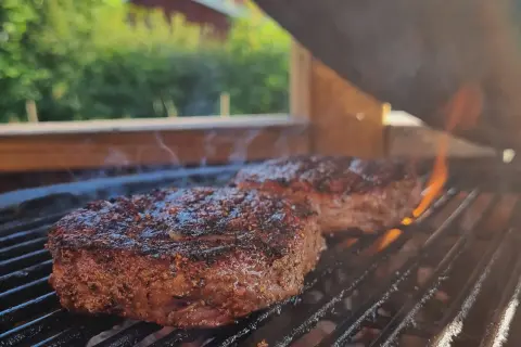 Två saftiga biffar med kryddor grillas över glödande kol. Perfekt för en sommarfest, undrar vad man kan grilla mer?