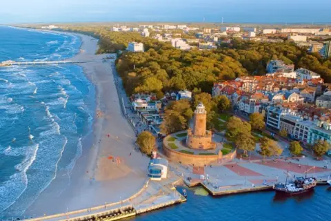 Widok z lotu ptaka na polski kurort nad morzem z latarnią morską, plażą i budynkami.
