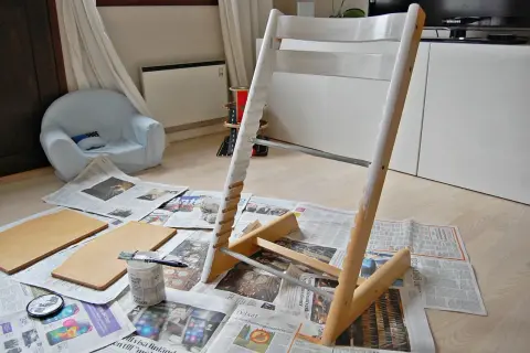 Måla om Stokke stol med vit färg. Trädelar och pensel ligger på tidningspapper.