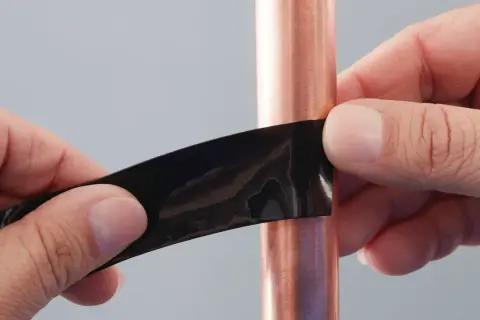 Hände dichten mit schwarzem Klebeband ein kleines Loch in einer Kupferwasserleitung ab.