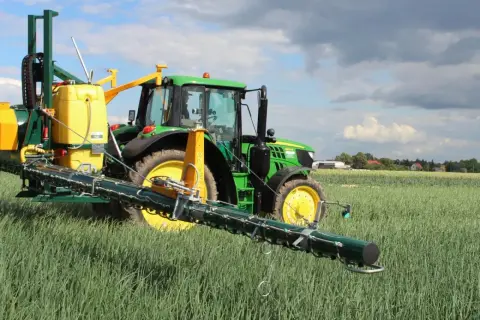 Zielony traktor z opryskiwaczem na polu. Warto sprawdzić movento 100 sc dawkowanie dla optymalnych rezultatów.