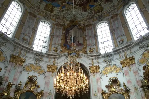 Prunkvoller Kronleuchter unter einer Decke mit Fresken, umgeben von opulenten Verzierungen, die die **Rokoko Architektur** widerspiegeln.