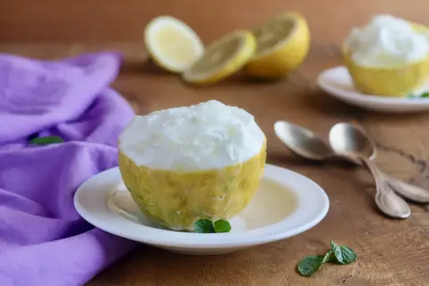 Sorbetto al limone senza albume servito in un limone scavato, con limoni affettati e un tovagliolo viola sullo sfondo.