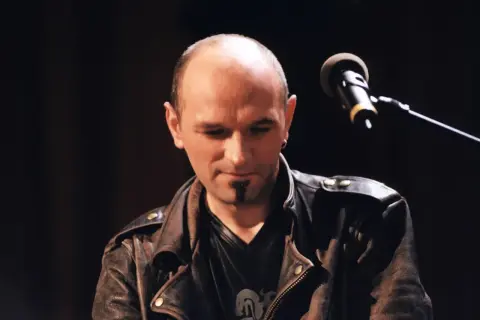 Artysta w skórzanej kurtce, z mikrofonem przed sobą. To jego pierwsze wykonanie, które warto przeżyć samemu.