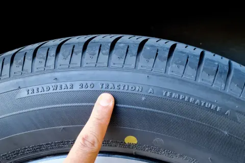 Palec wskazuje na oznaczenie "TREADWEAR 260 TRACTION A TEMPERATURE A" na oponie, informujące o jej właściwościach i dacie produkcji.