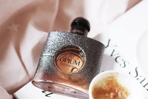 Błyszcząca butelka Black Opium od YSL, z nutą **opium floral shock**, obok filiżanki kawy i książki.