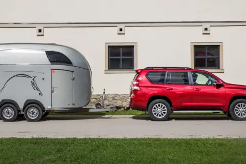 Czerwony SUV ciągnie przyczepę z koniem.