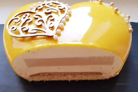 Entremet cœur jaune vif, décoré d'une arabesque dorée et de perles. La coupe révèle des couches onctueuses et un insert caramel beurre salé.