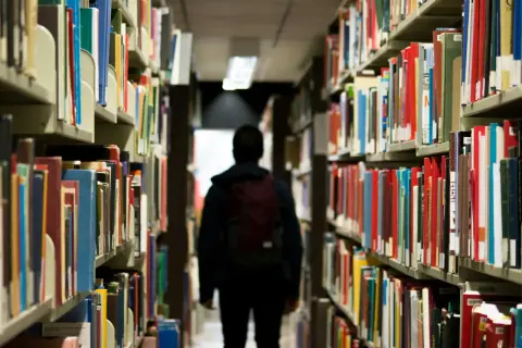 Ein Schüler mit Rucksack geht durch eine Bibliothek. Vielleicht sucht er nach Büchern, die ihm zeigen, dass das Gymnasium viel schwerer als Realschule ist.