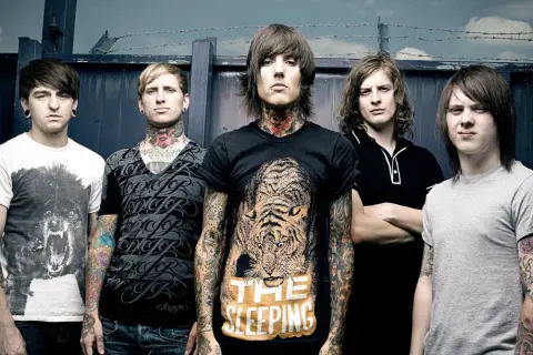 Bring Me The Horizon członkowie, z tatuażami i kolczykami, pozują przed ciemnym tłem.