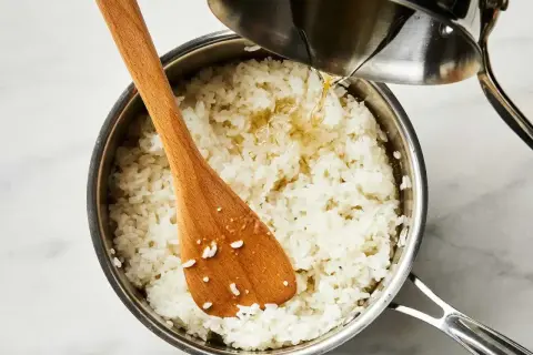 Gotowy ryż do sushi w garnku, do którego dodawany jest sos. Drewniana łyżka miesza ziarna.