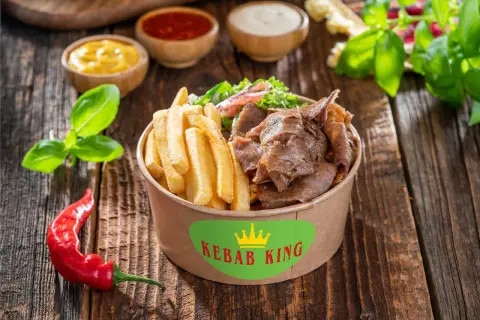 Kebab z frytkami i warzywami w pudełku Kebab King, obok sosów i papryczki chili.
