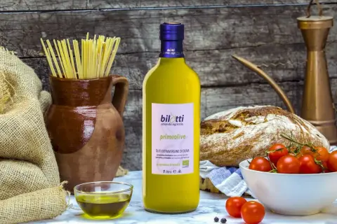Bottiglia di olio extravergine d'oliva Bilotti, con pasta, pane, pomodorini e una ciotolina di olio, per gustare i migliori tipi di olio.