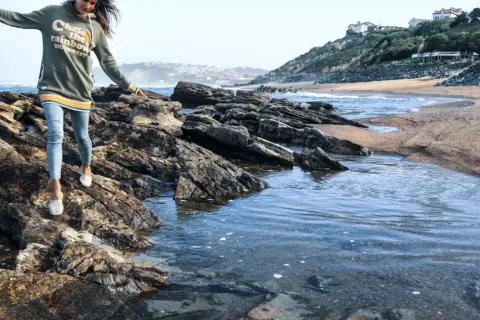 Une jeune femme profite d'une randonnée bord de mer, naviguant sur des rochers près de l'eau.