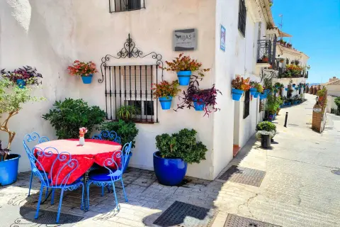 Mesa y sillas azules junto a pared blanca adornada con macetas. Un rincón encantador para descubrir qué ver en Mijas.