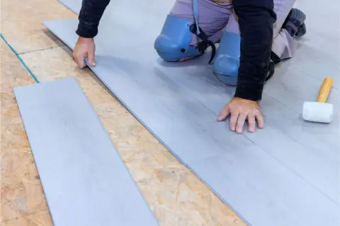 Instalación suelo laminado: un profesional coloca una tabla de suelo laminado gris sobre una base de madera contrachapada.