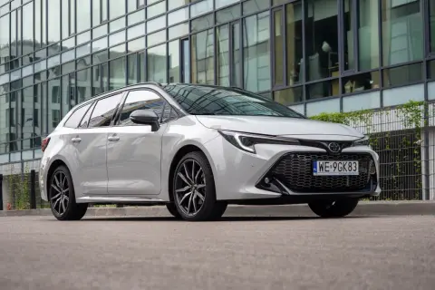 Biała Toyota Corolla 2.0 Hybrid na tle nowoczesnego budynku.