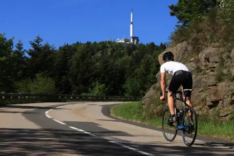 Cycliste en ascension vers le col de l'Oeillon, avec une tour de télécommunication visible au sommet.