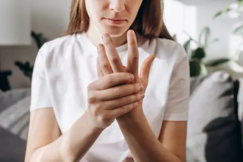 Kobieta masuje dłoń, cierpiąc z powodu bólu rąk w nocy.