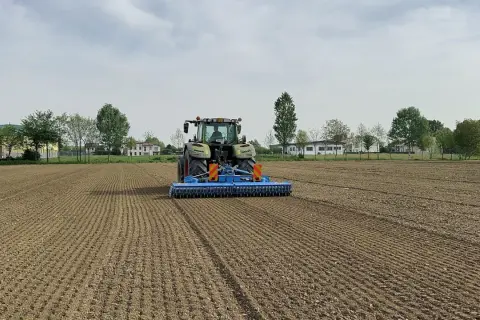 Trattore verde in azione per l'erpicatura del terreno, preparando il campo per la semina.