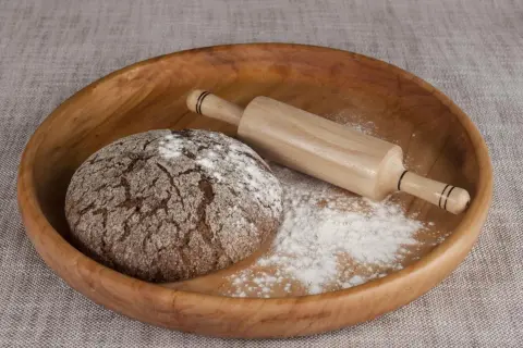 Drewniana miska z bochenkiem chleba, wałkiem i mąką. Czy pszenica durum ma gluten? Tak, zawiera go.