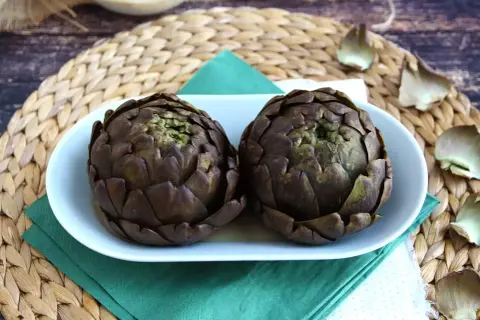 Deux artichauts violets sur une assiette blanche, prêts pour une recette d'artichaut savoureuse.