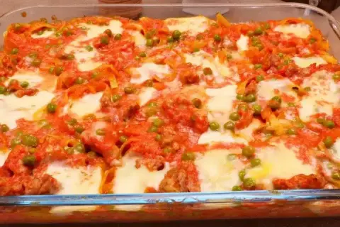 Nidi di tagliatelle al forno con ragù, piselli e mozzarella filante, un piatto invitante e saporito.