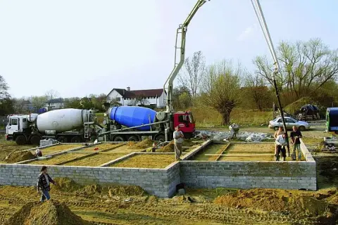 Betonowanie ławy fundamentowej. Dwie betoniarki i pompa do betonu pracują na budowie.