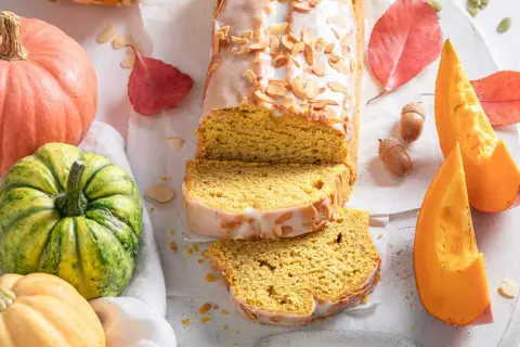 Bizcocho de calabaza Thermomix cubierto de glaseado y almendras. Rodeado de calabazas, hojas de otoño y bellotas.