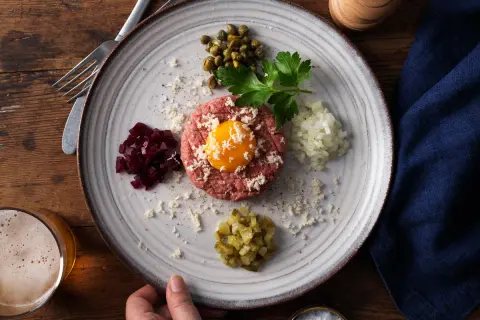 En tallrik med råbiff, äggula, kapris, hackad lök, rödbetor och gurka. Perfekt för ett klassiskt råbiff recept.