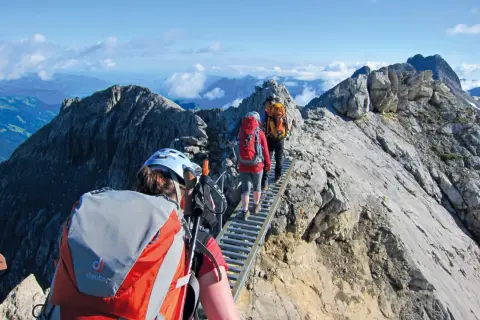 Drei Wanderer auf einer Hängebrücke während einer 5-tägigen Alpenwanderung. Die Aussicht ist atemberaubend.