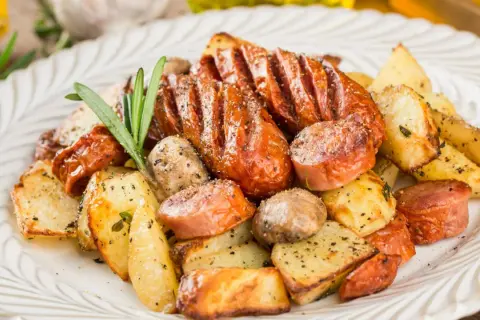 Pyszne dania z piekarnika na obiad: pieczone ziemniaki, kiełbaski i grzyby, doprawione ziołami i pieprzem.