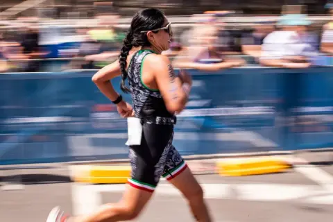 A woman in a triathlon suit, her hair in braids, runs with determination. This is the essence of Ironman training.
