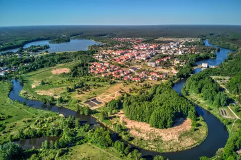 Malownicze miasteczko z czerwonymi dachami rozciąga się nad krętą rzeką, otoczone zielonymi lasami i polami.