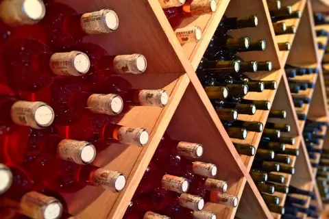 Scaffale in legno con bottiglie di vino rosse e scure, disposte con la corretta inclinazione per la conservazione.