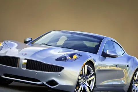 Srebrny Fisker Karma z charakterystycznym grillem i reflektorami, lśniącym lakierem i stylowymi felgami.