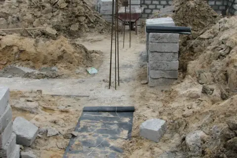 Budowa domu w toku. Widać wykopy, zbrojenie i materiały budowlane. To dopiero początek prac nad fundamentem.