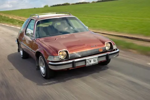 En brun AMC Pacer SC kör på en landsväg, med gröna fält som sträcker sig längs vägen.
