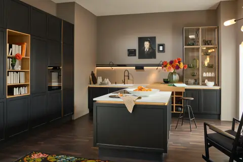 Cucina moderna con mobili neri e dettagli dorati, un'isola centrale con frutta e un tappeto dai colori caldi che aggiunge un tocco accogliente.