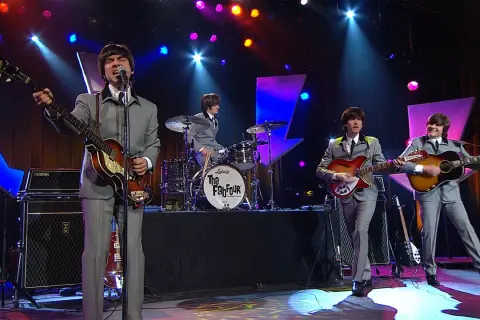 Una cover band sul palco, con abiti grigi e chitarre, ricorda i Fab Four.