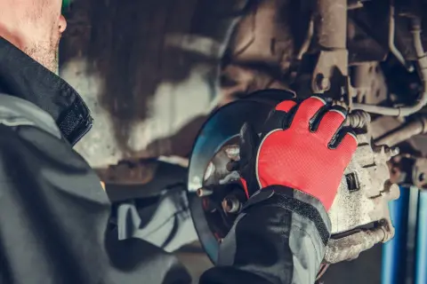 Mechanik w czerwonych rękawicach pracuje przy hamulcach, przygotowując wymianę przewodów hamulcowych.