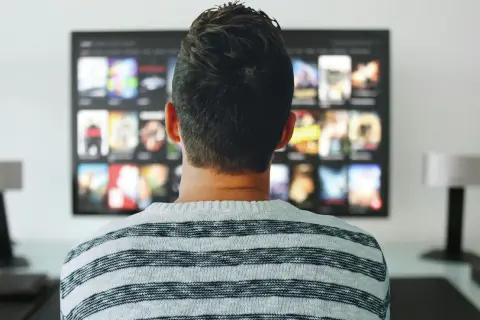 Mężczyzna w pasiastym swetrze ogląda na telewizorze menu aplikacji, gdzie widnieje logo Orange TV.
