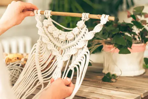 Mains créatives travaillant sur une décoration murale en macramé. Une belle idée déco macramé pour un intérieur bohème.