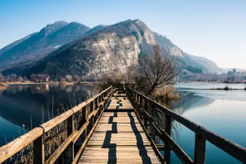 Passerella in legno su lago calmo, montagne sullo sfondo. Un luogo incantevole per scoprire cosa vedere in Franciacorta.